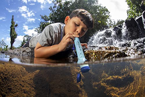 A young boy is drinking water through a LifeStraw Personal Water Filter for Hiking, Camping, Travel, and Emergency Preparedness in the water.